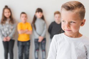 Un niño pequeño con camiseta blanca mirando hacia un lado, con otros niños desenfocados detrás de él. ¿Los problemas de integración sensorial pueden darse en cualquier niño? qué es la integración sensorial