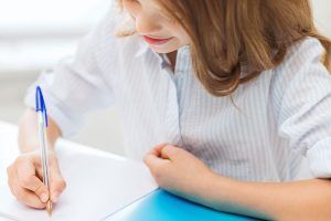 Niña con camisa a rayas escribiendo en un papel con un bolígrafo azul. ¿Qué es la integración sensorial?