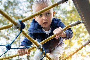 Un niño con chaqueta azul escalando una estructura de cuerdas en un parque. ¿Qué ocurre cuando hay problemas?, ¿qué es la integración sensorial?