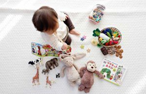 Un niño pequeño juega en una manta con juguetes educativos variados, como animales de plástico, frutas de tela y un libro ilustrado. Juguetes para niños de 0 a 3 años