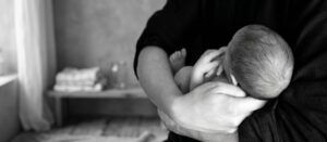 Un adulto acuna a un recién nacido en sus brazos en el interior de una casa; la imagen, en blanco y negro y con un fondo desenfocado, plasma de forma preciosa la ternura que a menudo se comparte con los bebés prematuros.
