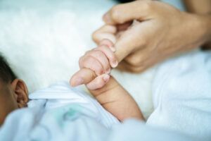 Un primer plano de un bebé, que representa a los bebés prematuros, sujetando con delicadeza el dedo de un adulto mientras ambos descansan sobre una suave superficie blanca.
