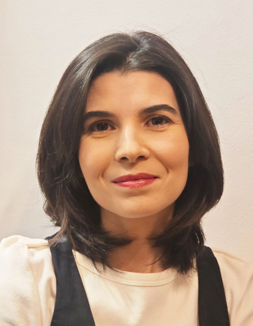 Mujer con el pelo oscuro hasta los hombros y piel clara, vestida con un top color crema y una camiseta negra sin mangas, mirando a la cámara con expresión neutra sobre un fondo liso y claro: perfecta para una foto de presentación o de perfil en la sección «Sobre mí».