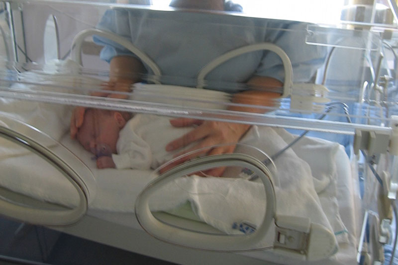 Las manos de una persona se asoman por las aberturas de una incubadora para acariciar con delicadeza a un recién nacido que descansa en su interior. Secuelas neurológicas o de aprendizaje a largo plazo en un bebé prematuro